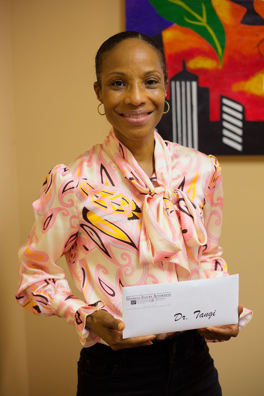 A woman in a pink shirt is holding a check in front of a painting