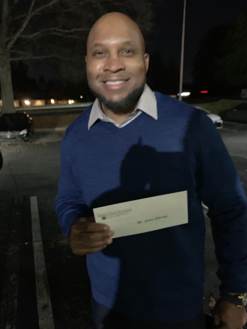 A man in a blue sweater is holding a check