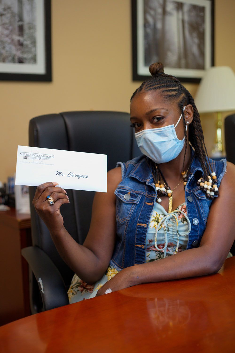 A woman wearing a mask is sitting at a desk holding a check