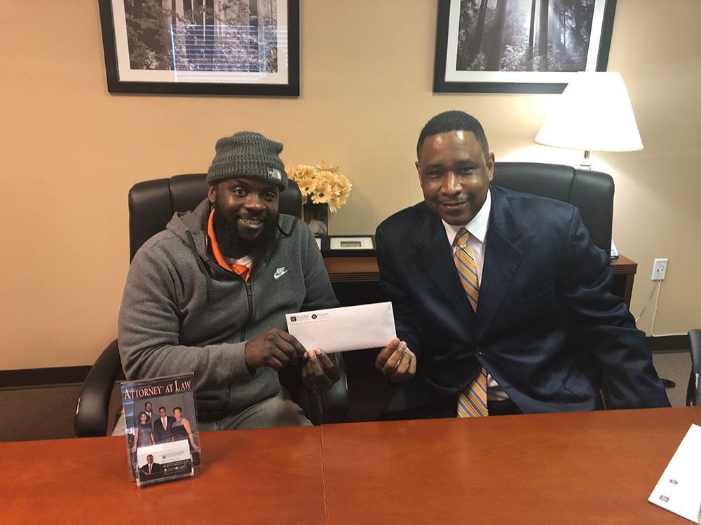 Two smiling men are sitting at a table holding a check