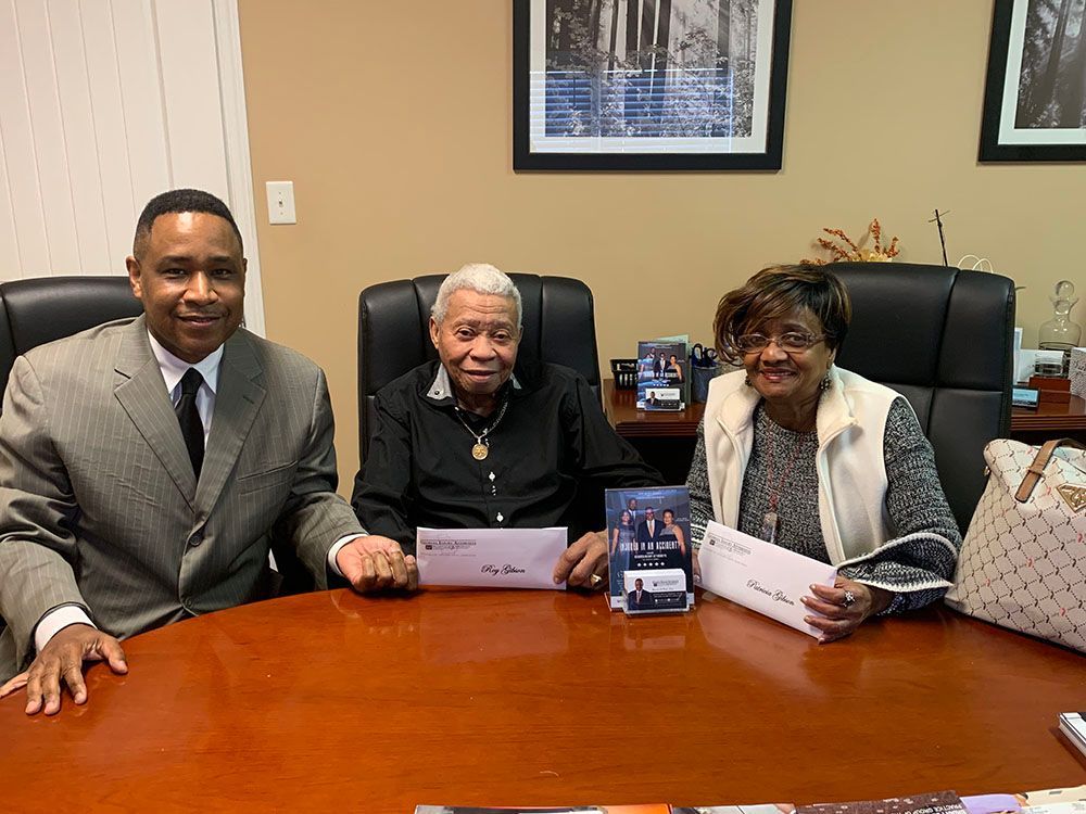 Brian D. Poe, Esq. is sitting at a table with two happy clients