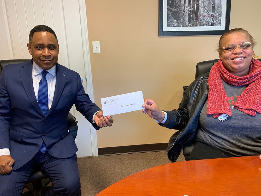 Brian D. Poe, Esq. is handing a woman a check