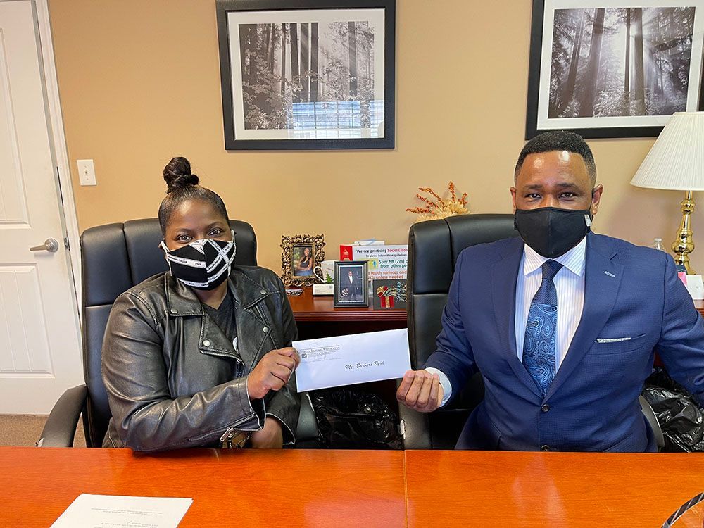Brian D. Poe, Esq. and a happy client wearing masks are sitting at a table holding a check