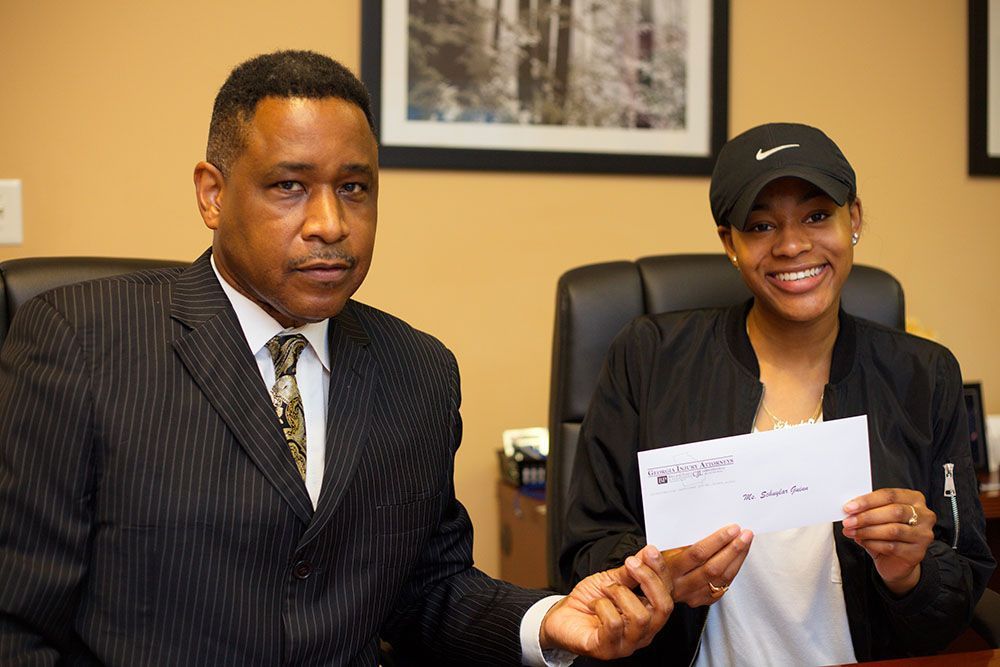 Brian D. Poe, Esq. and a smiling woman are sitting at a table holding a check