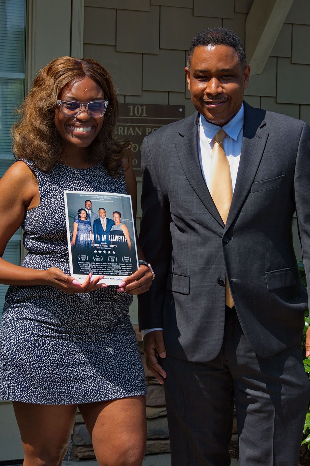 A man in a suit and tie stands next to a woman holding a flyer