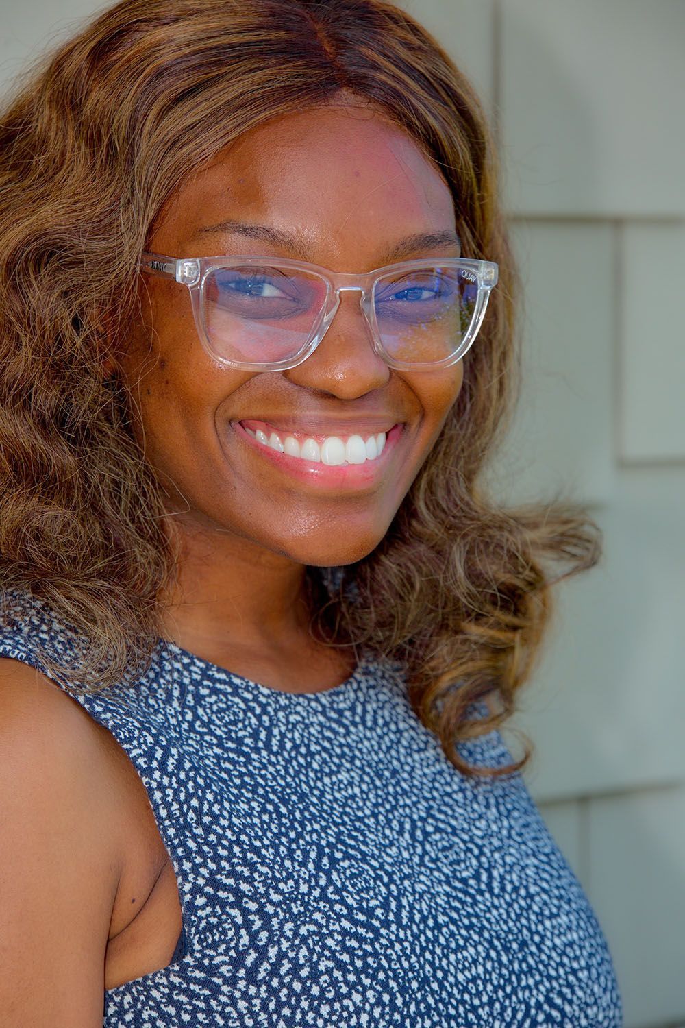 A woman wearing glasses and a blue dress is smiling for the camera