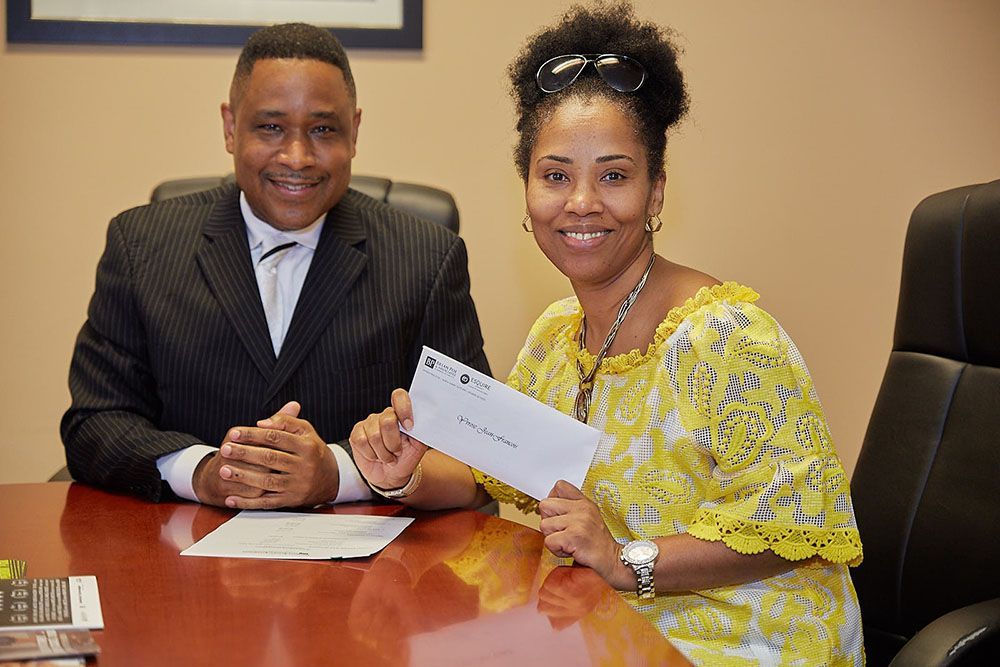 Brian D. Poe, Esq. and a smiling female client are sitting at a table holding a check