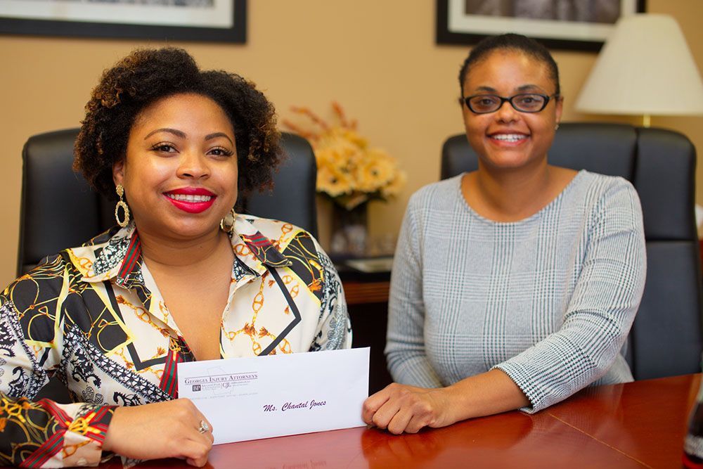 Two women are sitting at a desk holding an envelope