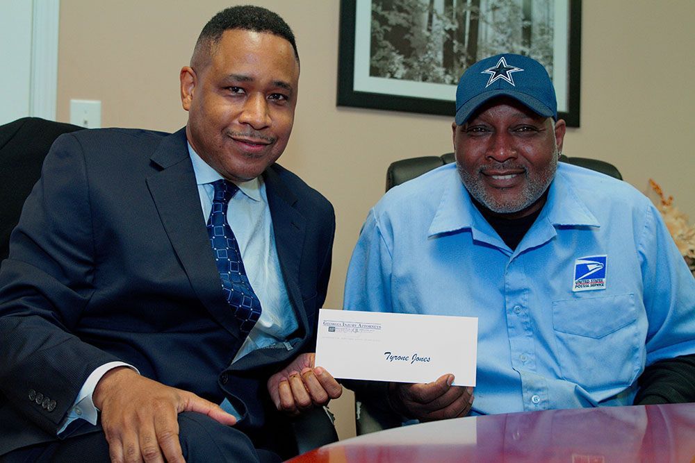 Brian D. Poe, Esq. is sitting next to a man in a blue shirt holding a check