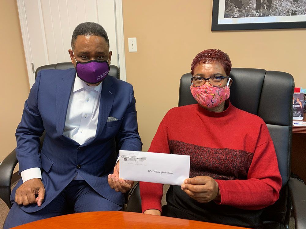 Brian D. Poe, Esq. and a woman wearing a red sweatshirt and a mask are sitting at a table holding a check