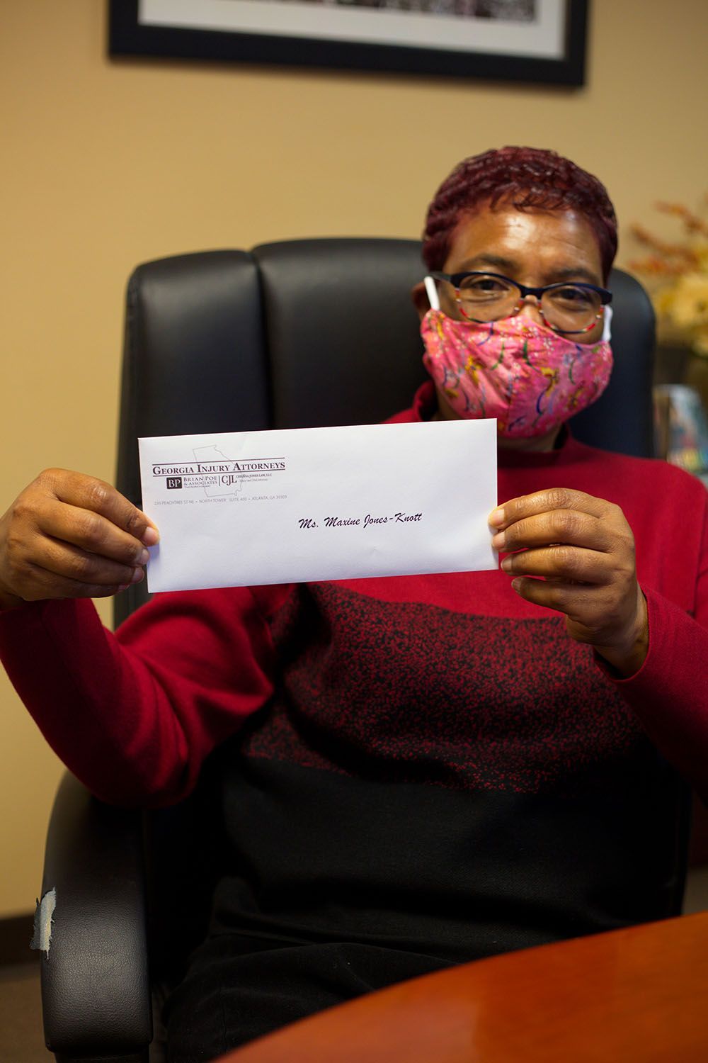 A client wearing a mask is sitting in a chair holding an envelope