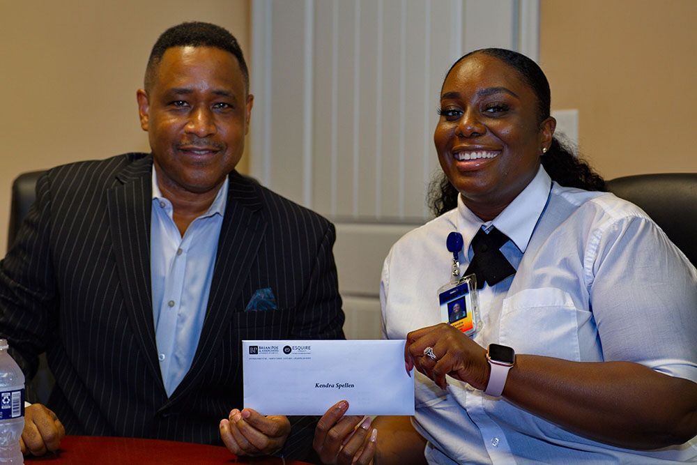 Brian D. Poe, Esq. and a woman in white are sitting at a table holding a check