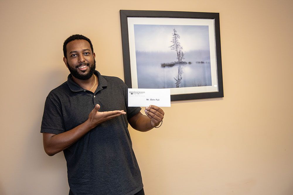 A man is holding a check in front of a picture on a wall