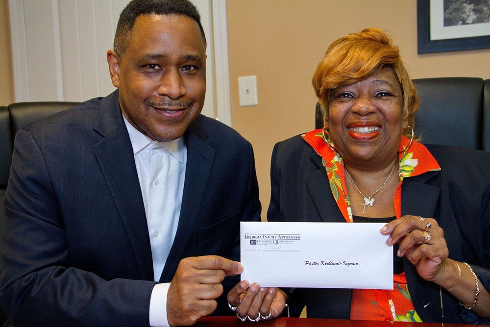 Brian D. Poe, Esq. and a cheerful female client are sitting at a table holding a check