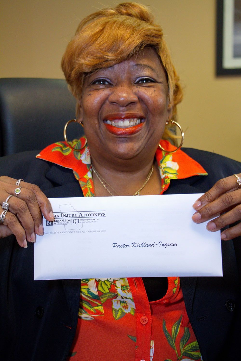 A woman is smiling while holding an envelope with a check on it