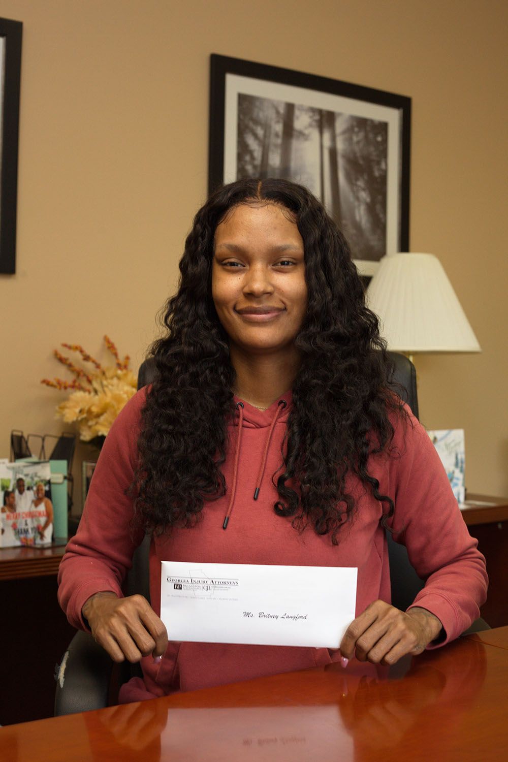 A woman with a long and curly hair is sitting at a desk holding a check