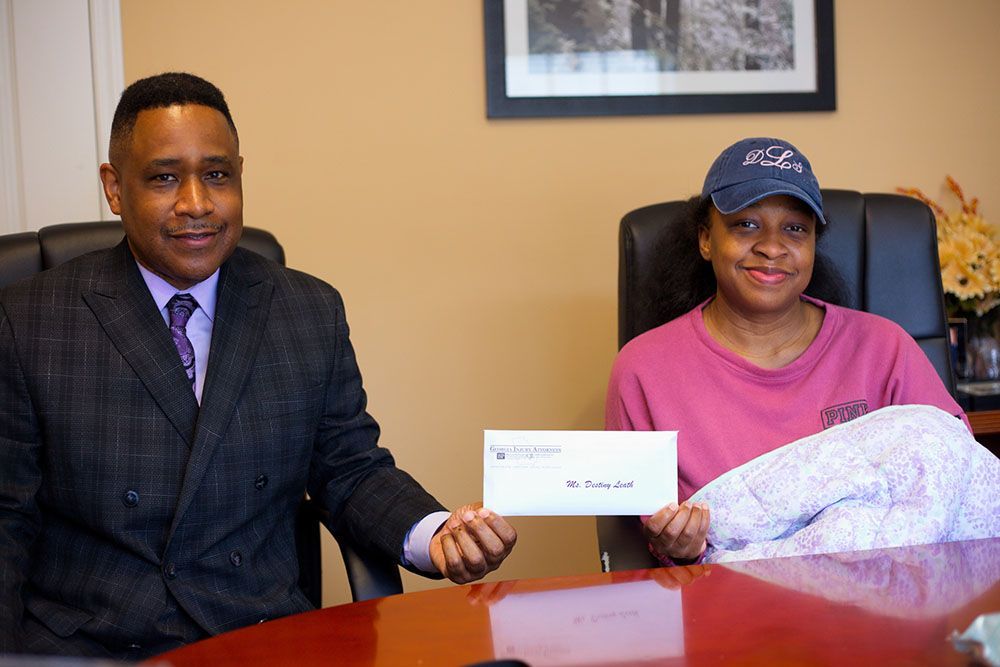 Brian D. Poe, Esq. and a joyful woman are sitting at a table holding a check