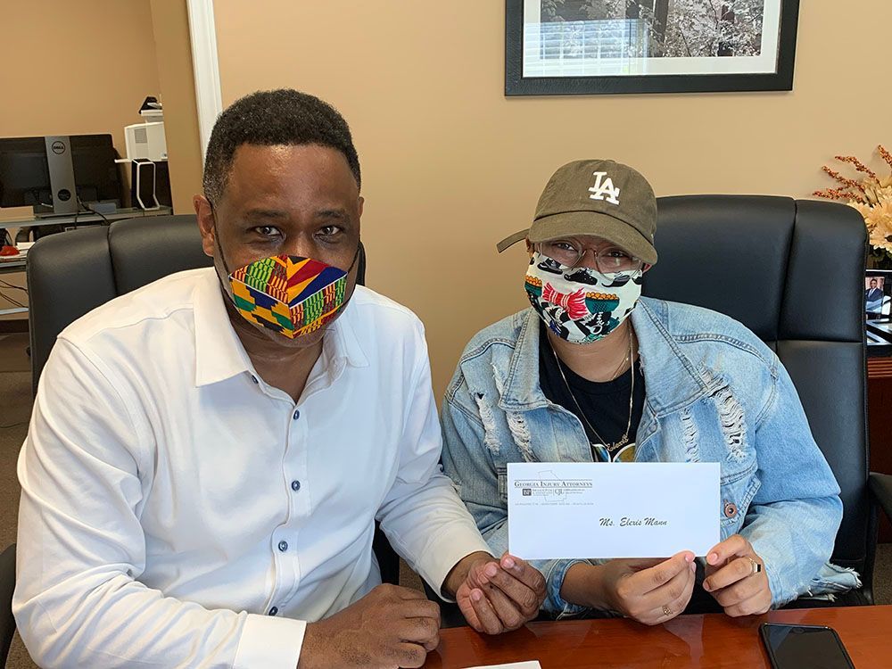 A man and a woman wearing masks are sitting at a desk holding a check