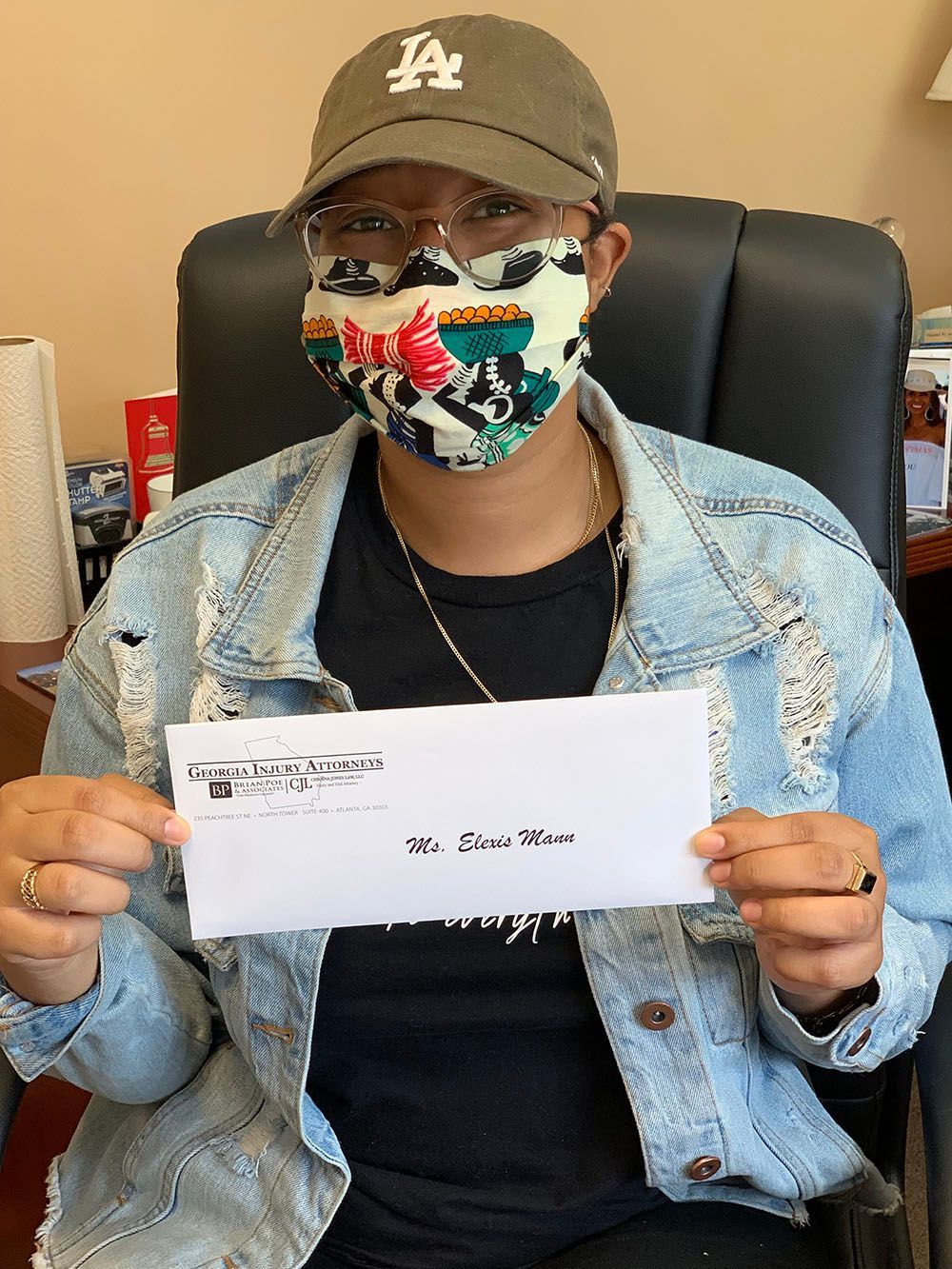 A woman wearing a hat and a mask is holding a check