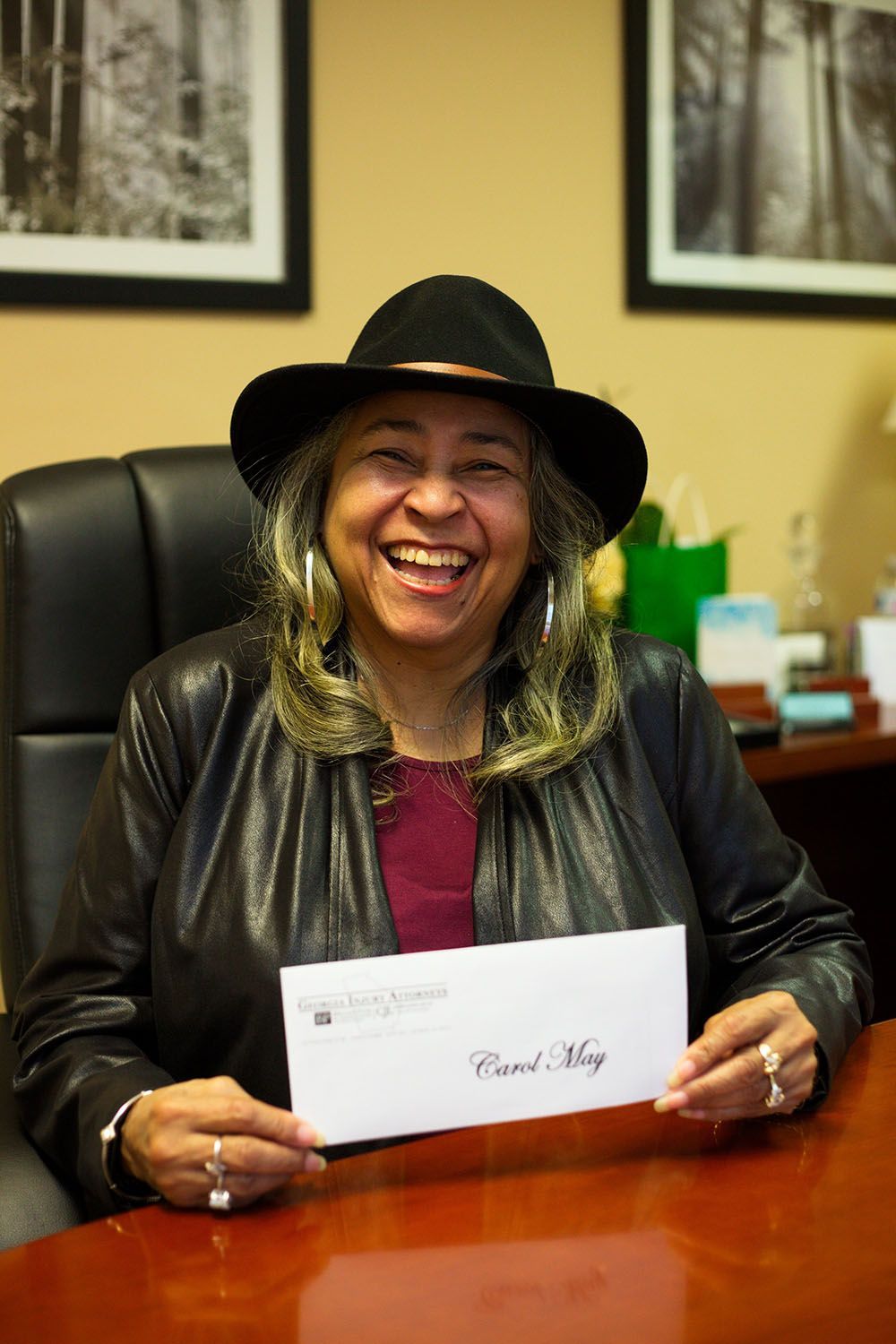 A woman in a hat is sitting at a desk holding a check