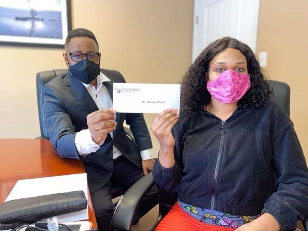 Brian D. Poe, Esq. and a woman wearing masks are holding a check