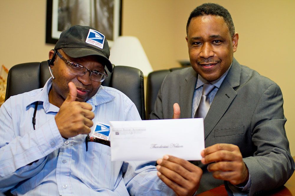 Two men are sitting at a table holding a check and giving a thumbs-up