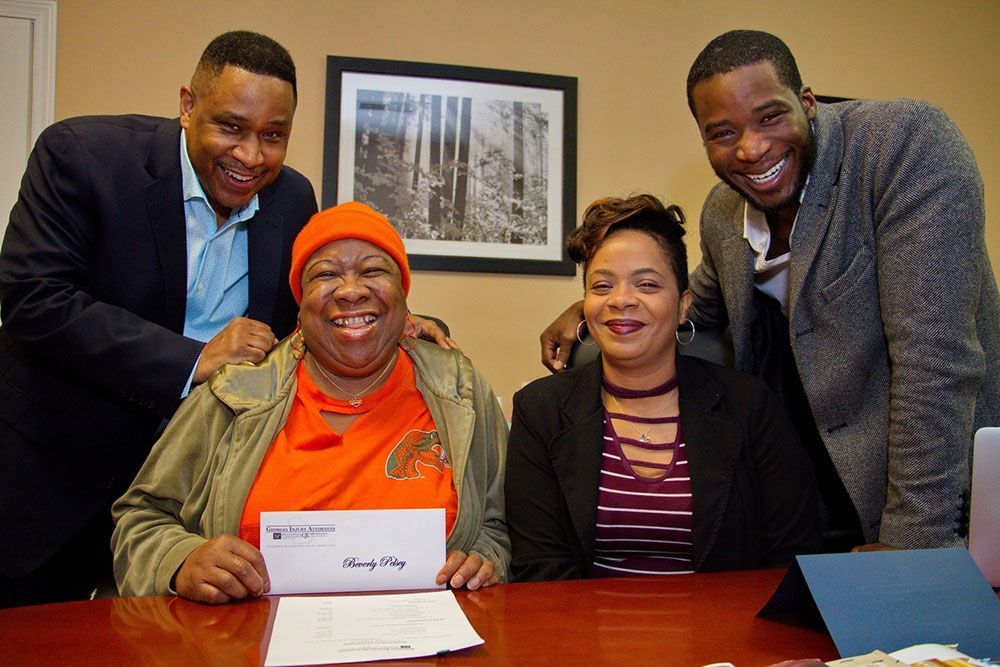 Georgia Injury Attorneys and a happy client wearing an orange beanie holding a check