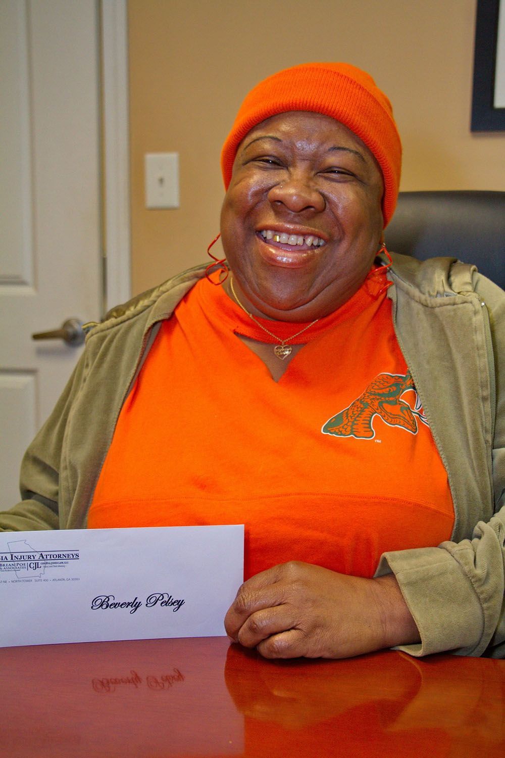 A woman in an orange shirt is smiling while holding a check