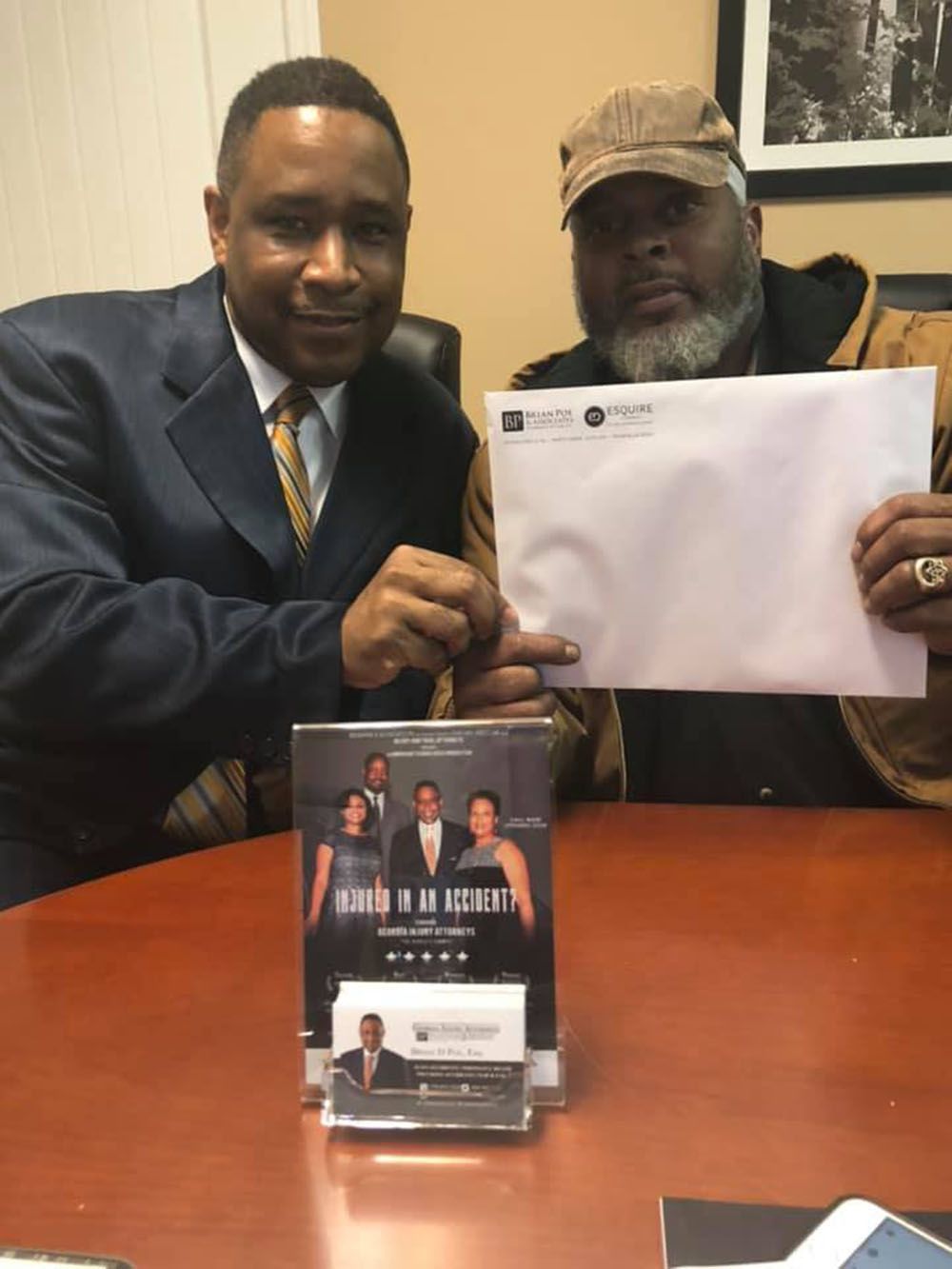 Brian D. Poe, Esq. and a man with a hat sitting at a table holding a check