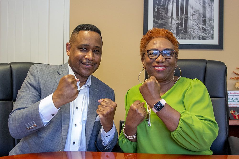 Brian D. Poe, Esq. and a woman are sitting at a table with their fists in the air