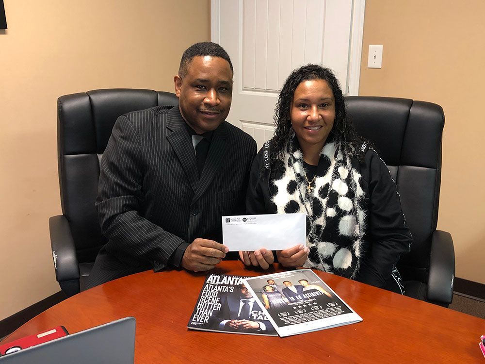 Brian D. Poe, Esq. and a joyful female client are sitting at a table holding a check