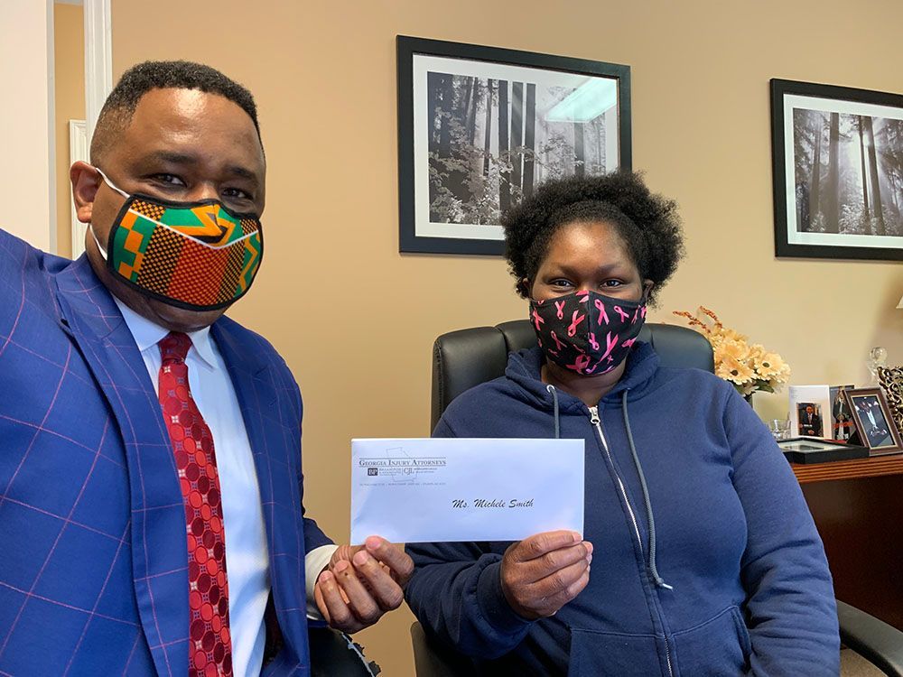 Brian D. Poe, Esq. and a woman wearing face masks are holding a check