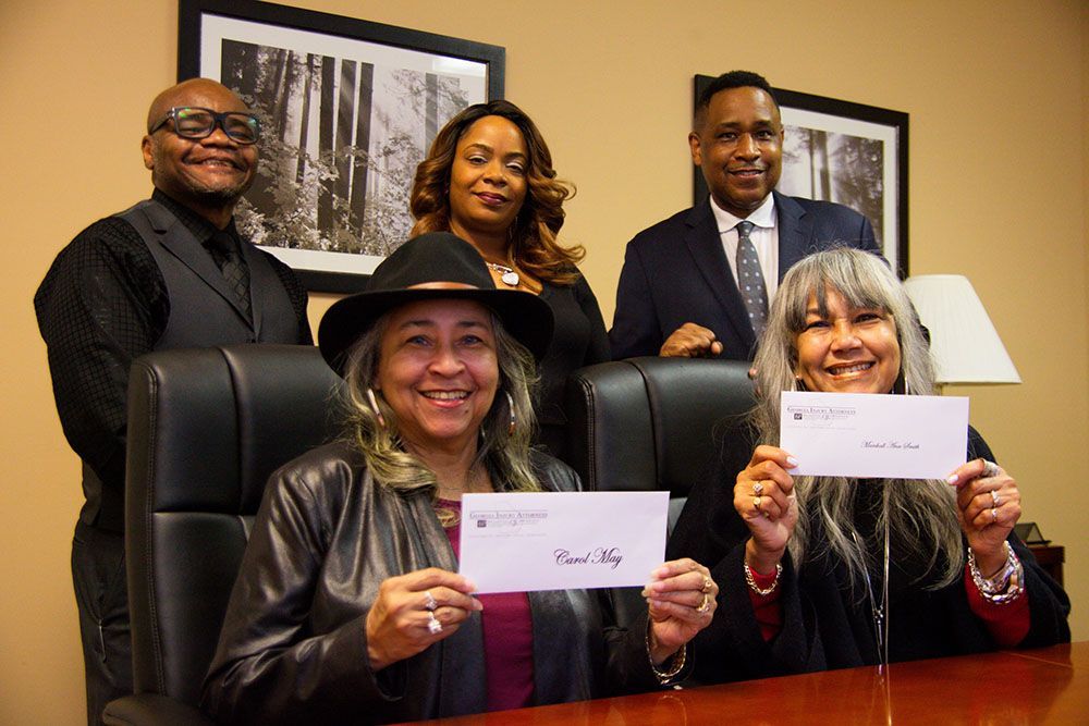 Georgia Injury Attorneys' happy clients are sitting at a table holding checks
