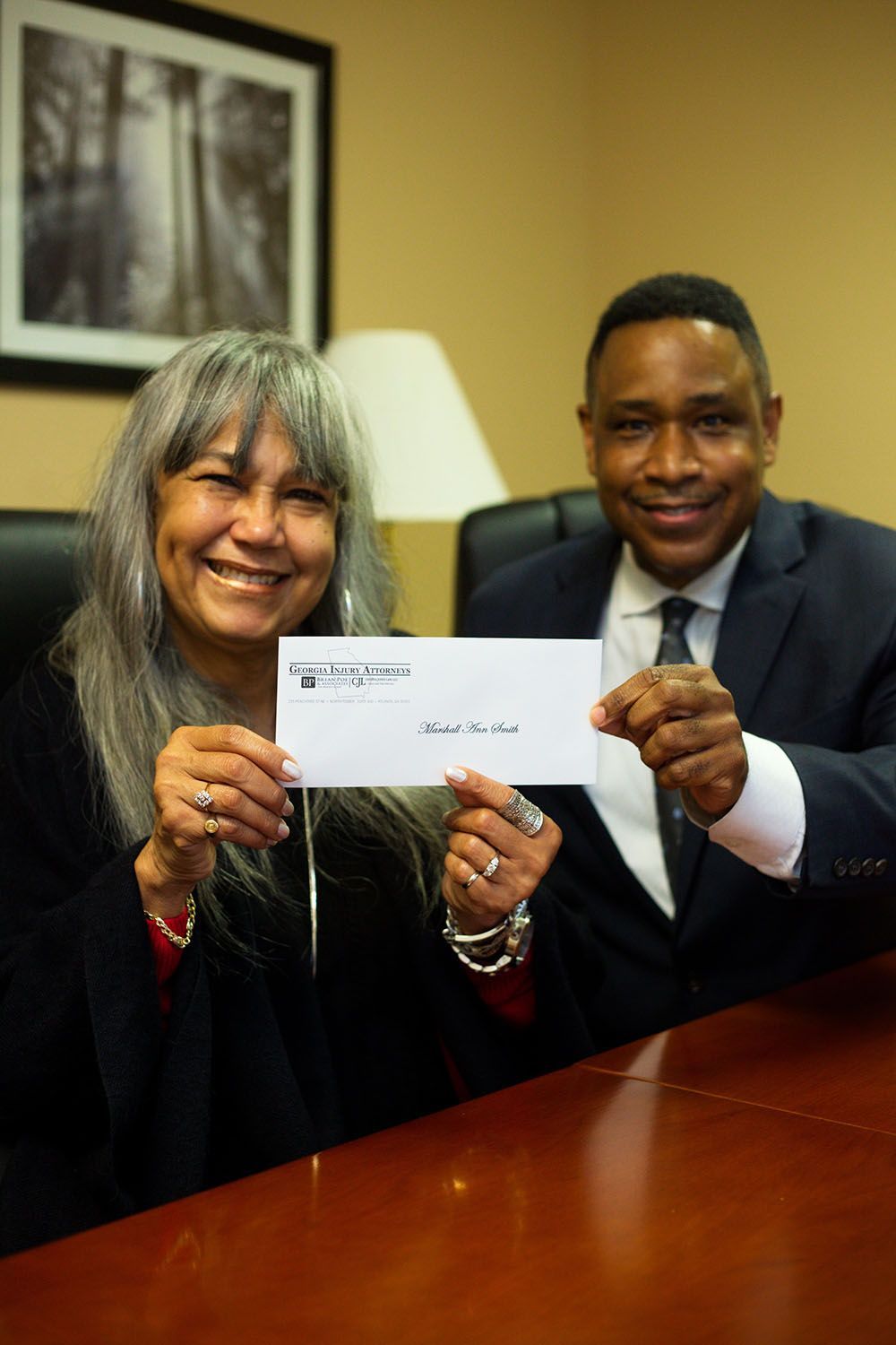 Brian D. Poe, Esq. and a woman are sitting at a table holding a check
