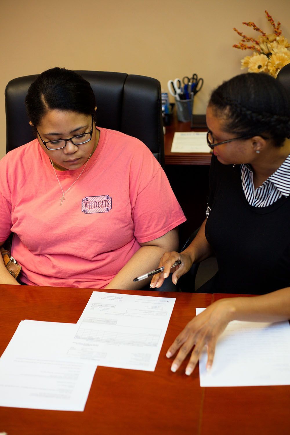 Two women are sitting at a desk looking at papers