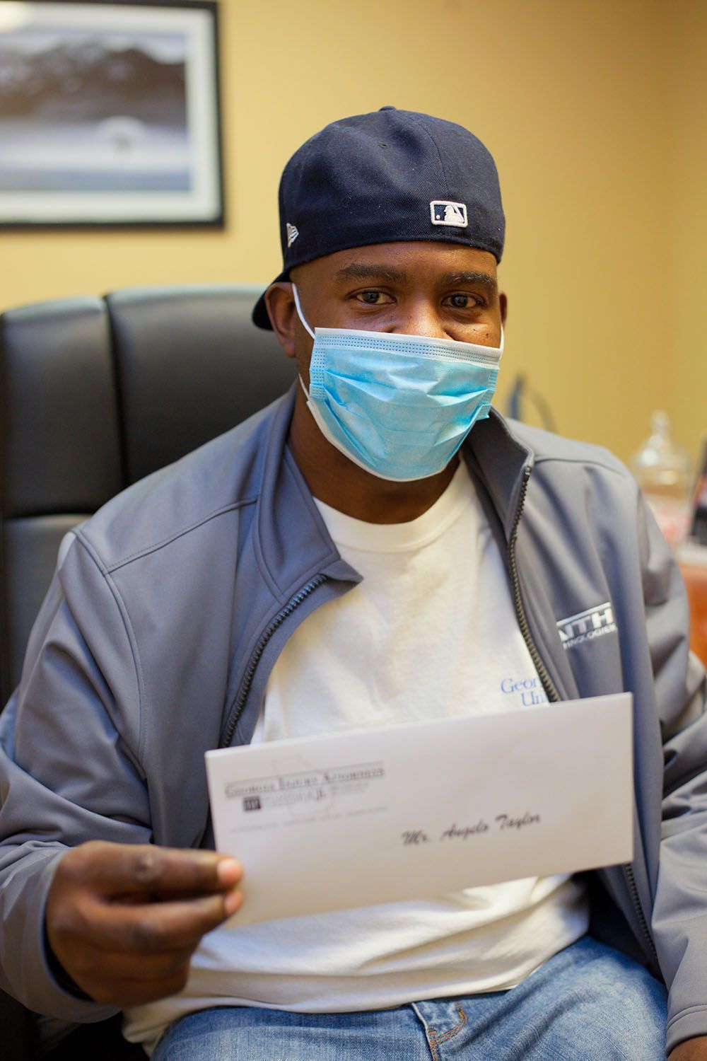 A man wearing a mask and a hat is holding a check