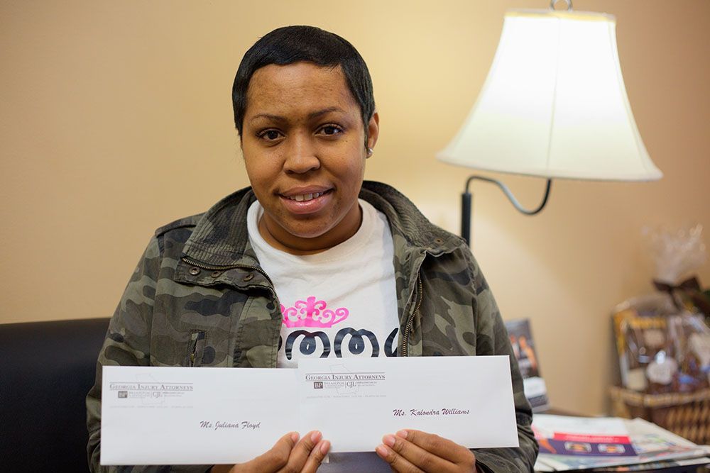 A woman in a camo jacket is holding 2 checks