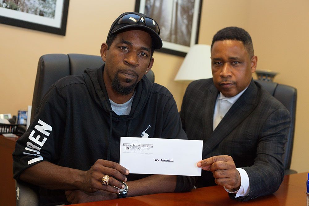 Brian D. Poe, Esq. and a man in a black hoodie with a hat is holding a check