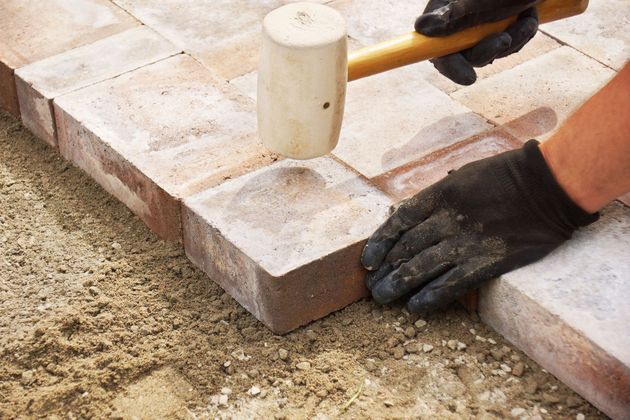 Hands wearing black gloves laying light gray paving stones around a white pipe