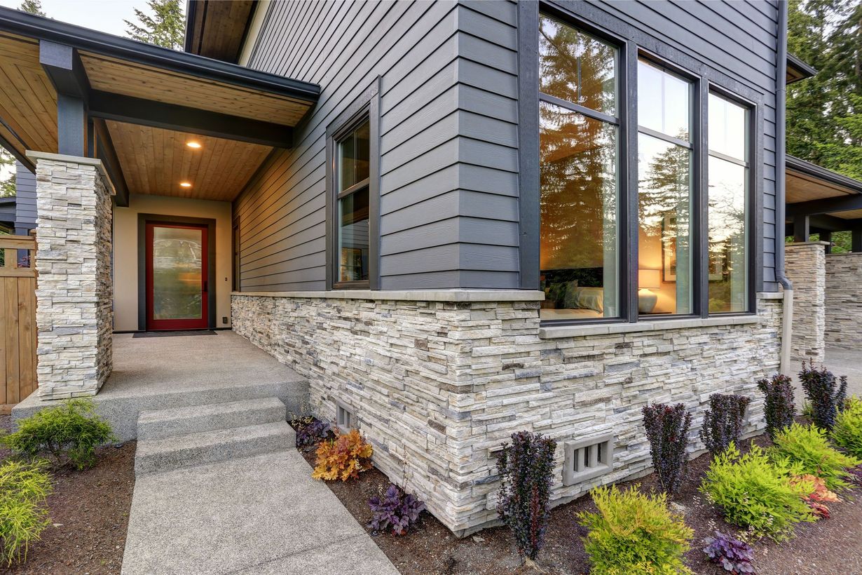 Modern home exterior with stone facade, ramped walkway, and large windows beside landscaped shrubs