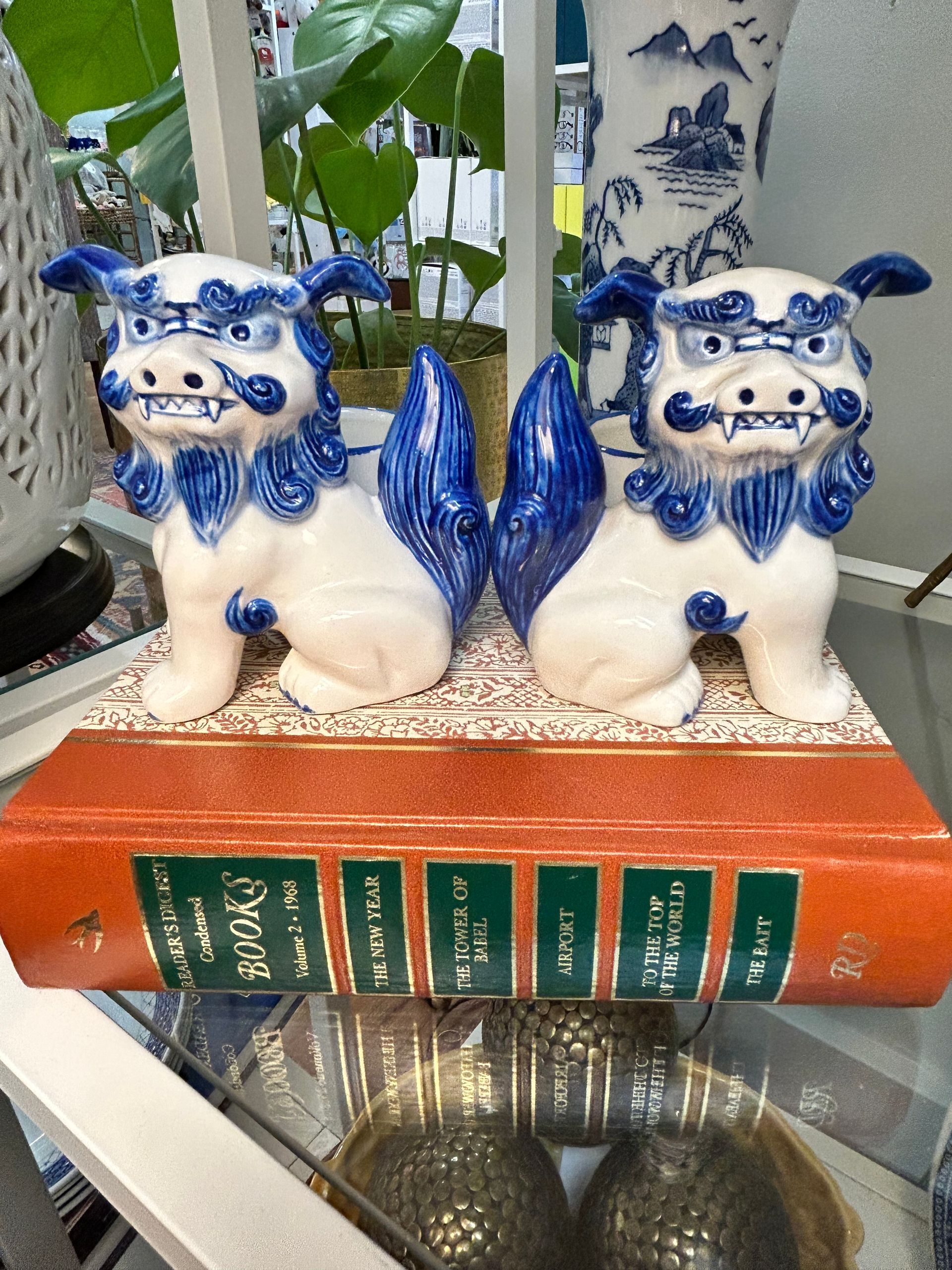 A pair of blue and white ceramic foo dog statues sit side-by-side on top of a thick, orange decorative book.