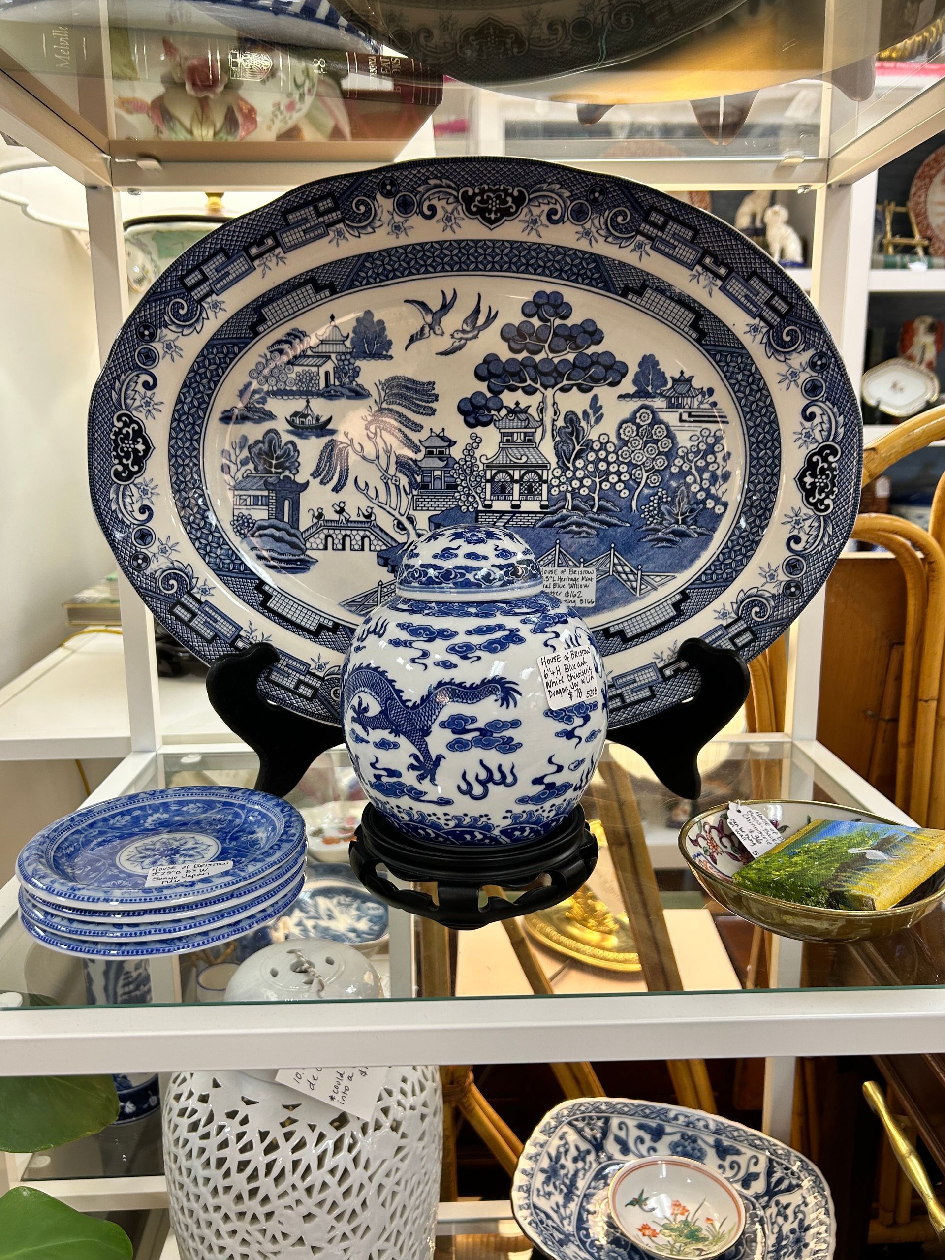 Blue and white patterned porcelain platters, small plates, and a decorative jar were displayed on a white shelving unit.