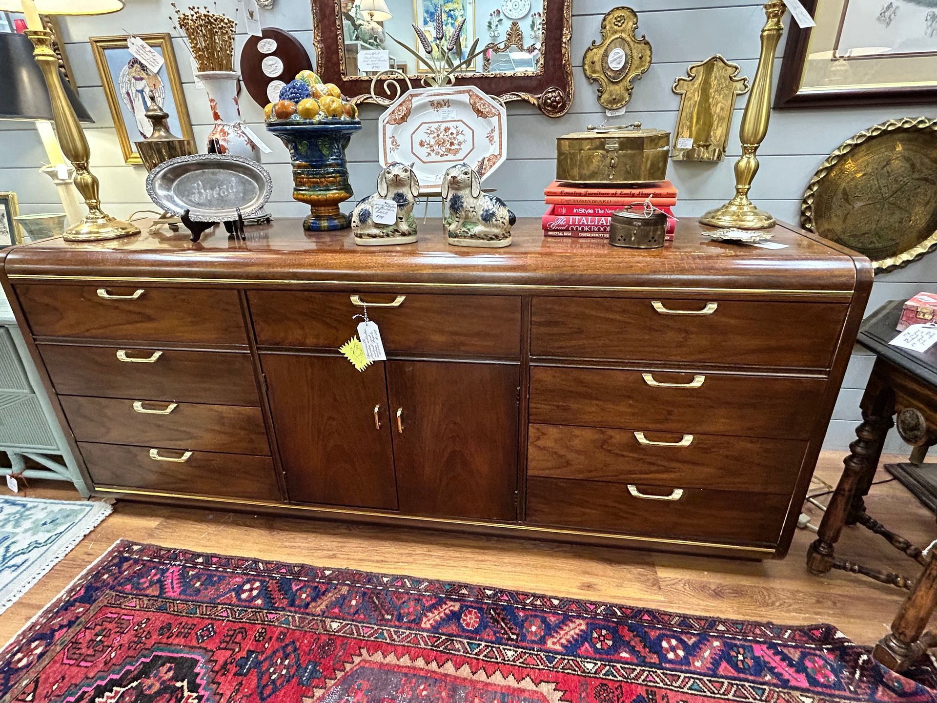 A long, mid-century modern wooden dresser with brass hardware, featuring six drawers and two central cabinet doors.
