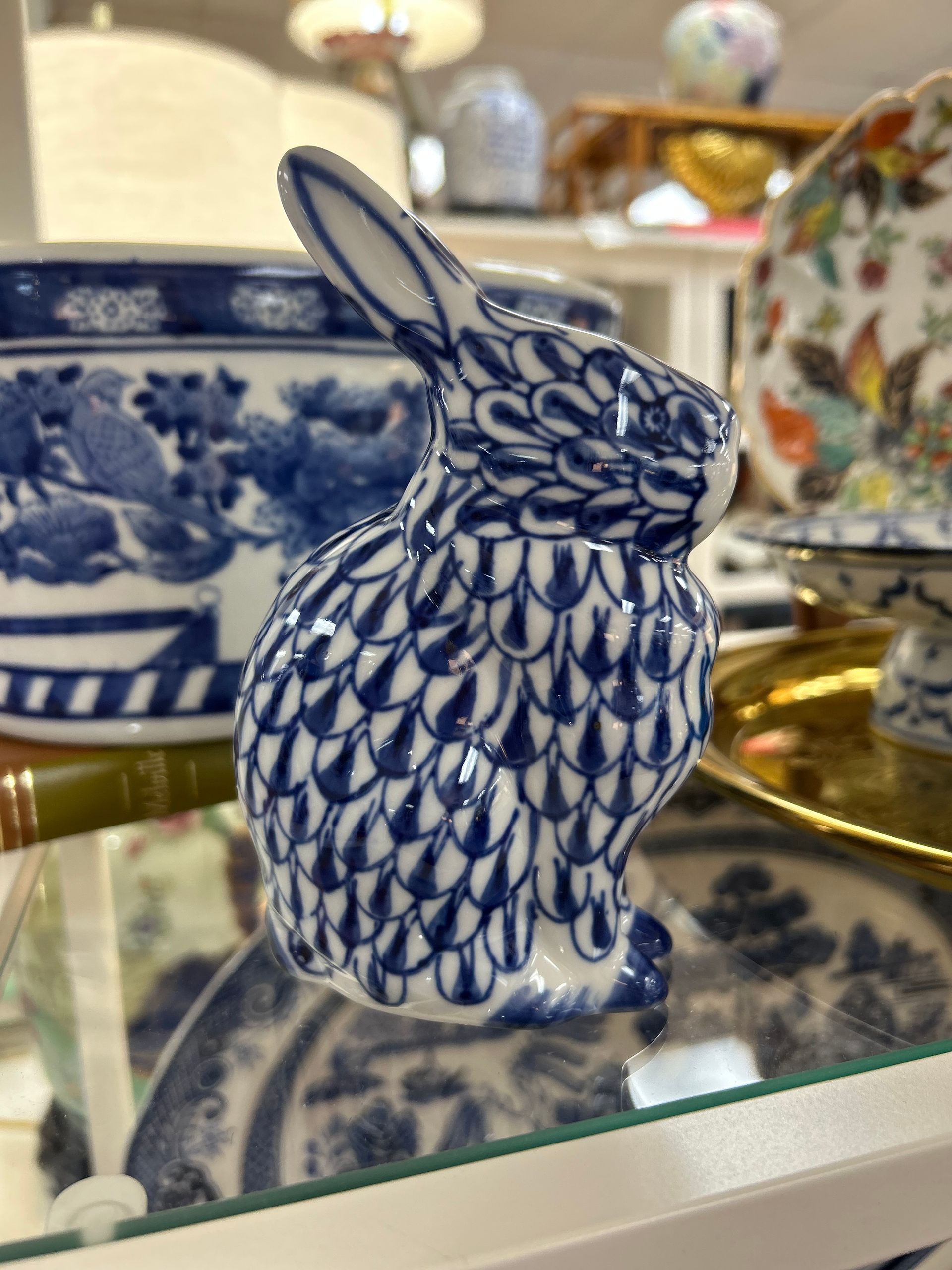 A blue and white porcelain rabbit figurine with a fish-scale pattern, sitting on a glass shelf in a retail setting.