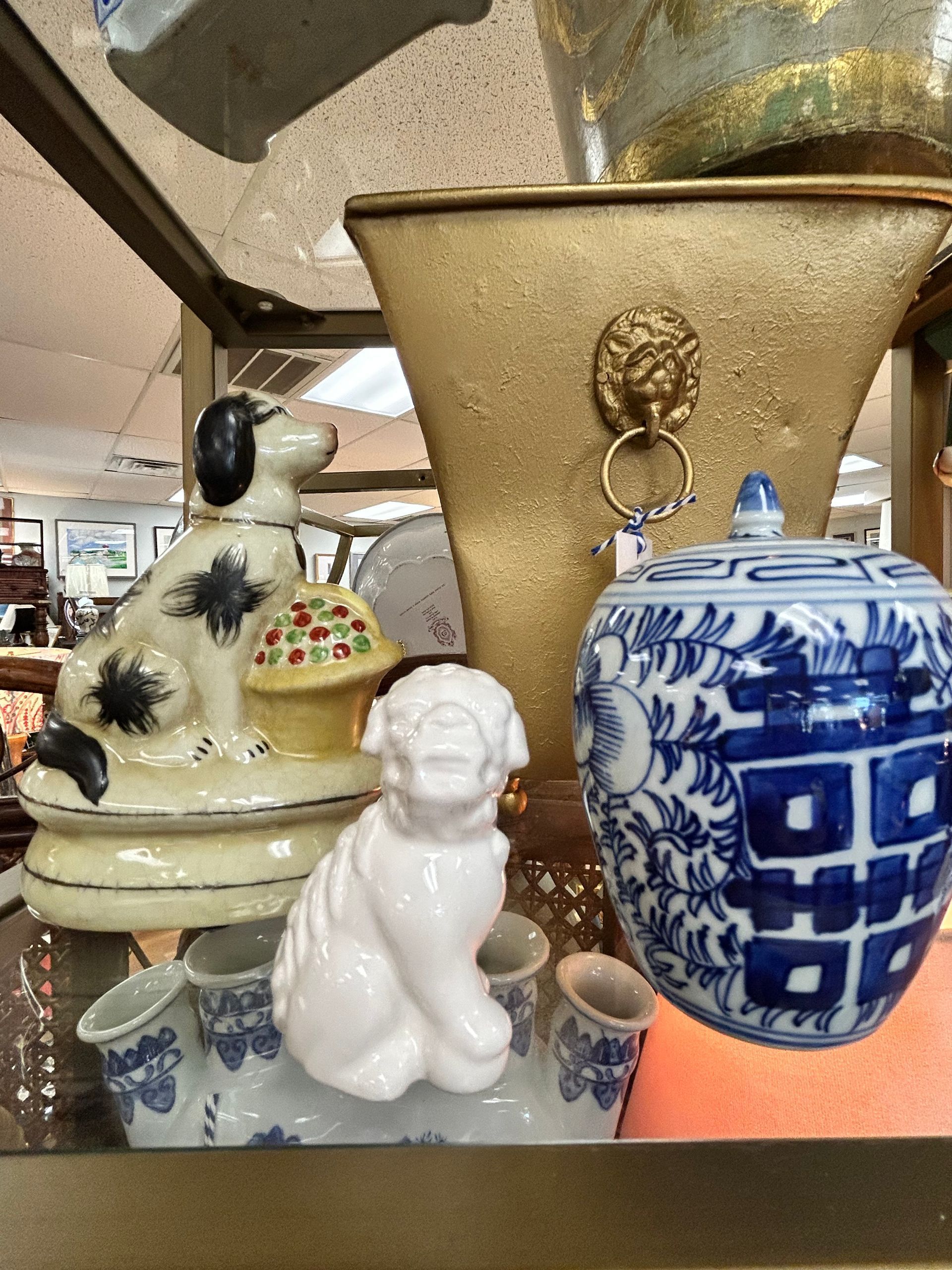 Ceramic dog figurines, a gold-toned container with a lion-head ring handle, and a blue and white patterned lidded jar.