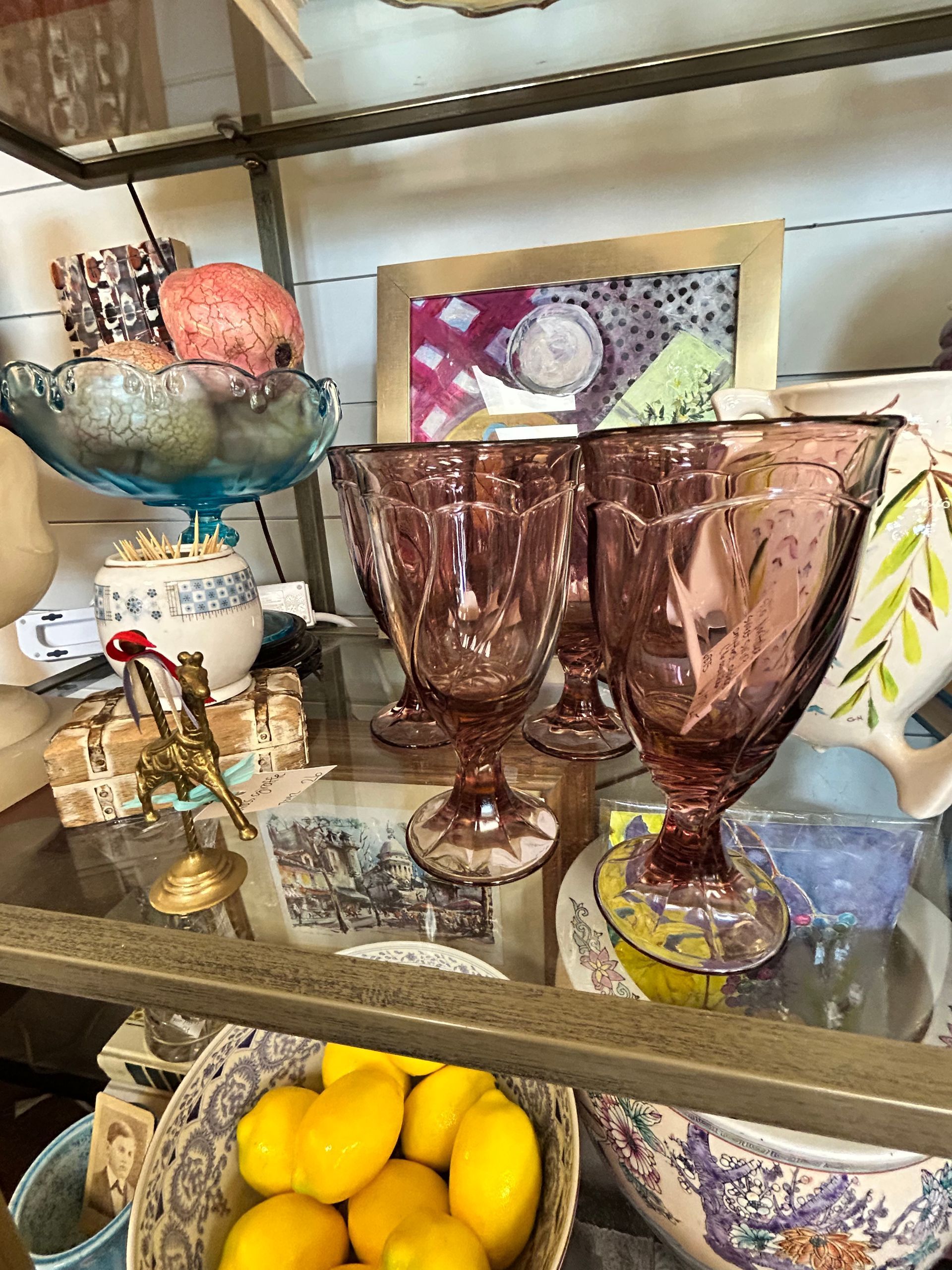 Display shelf featuring purple textured goblets, a bowl of lemons, a small brass horse, and decorative ceramic items.