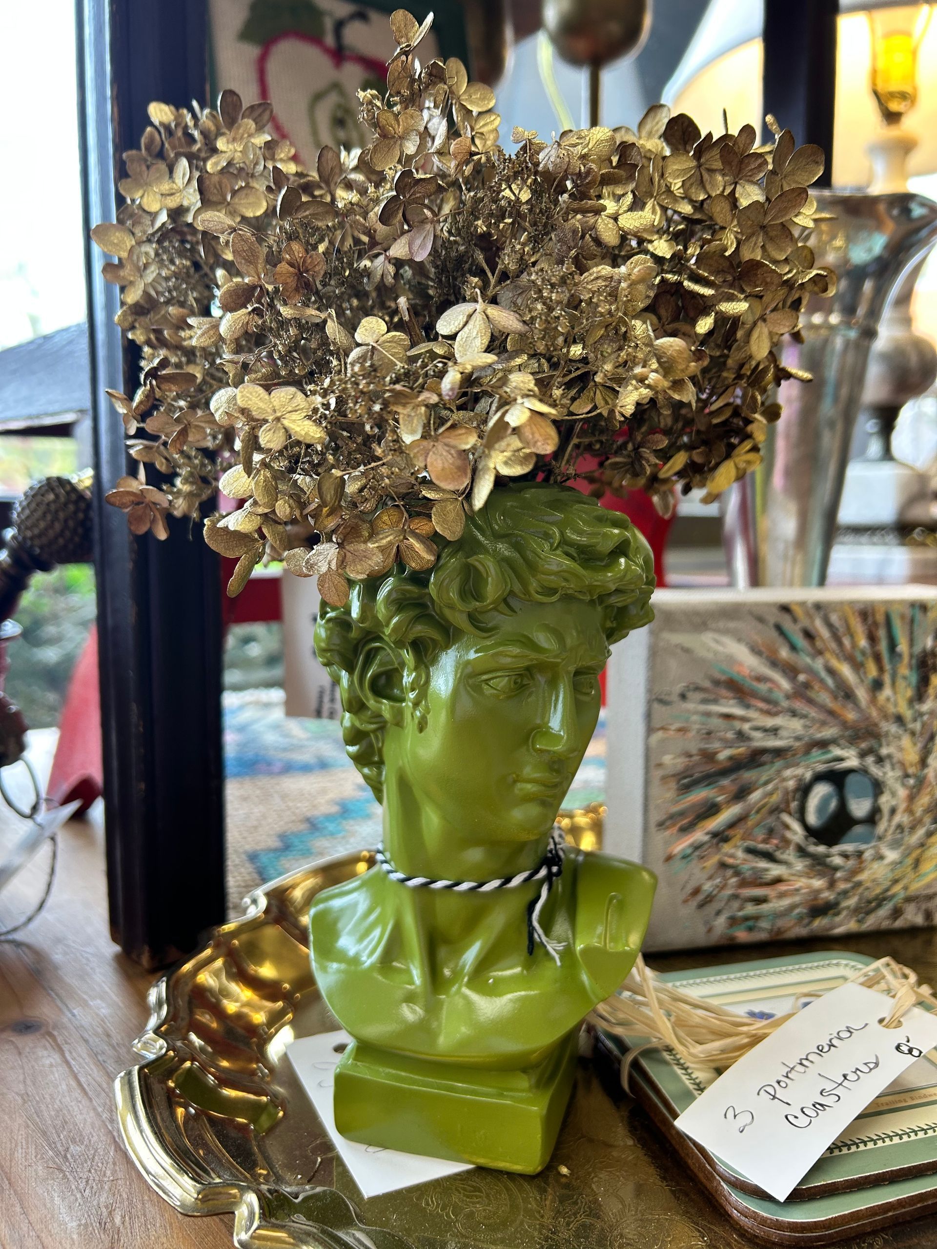 A lime green sculpture of a head used as a vase, filled with golden dried hydrangea, sitting on a table.