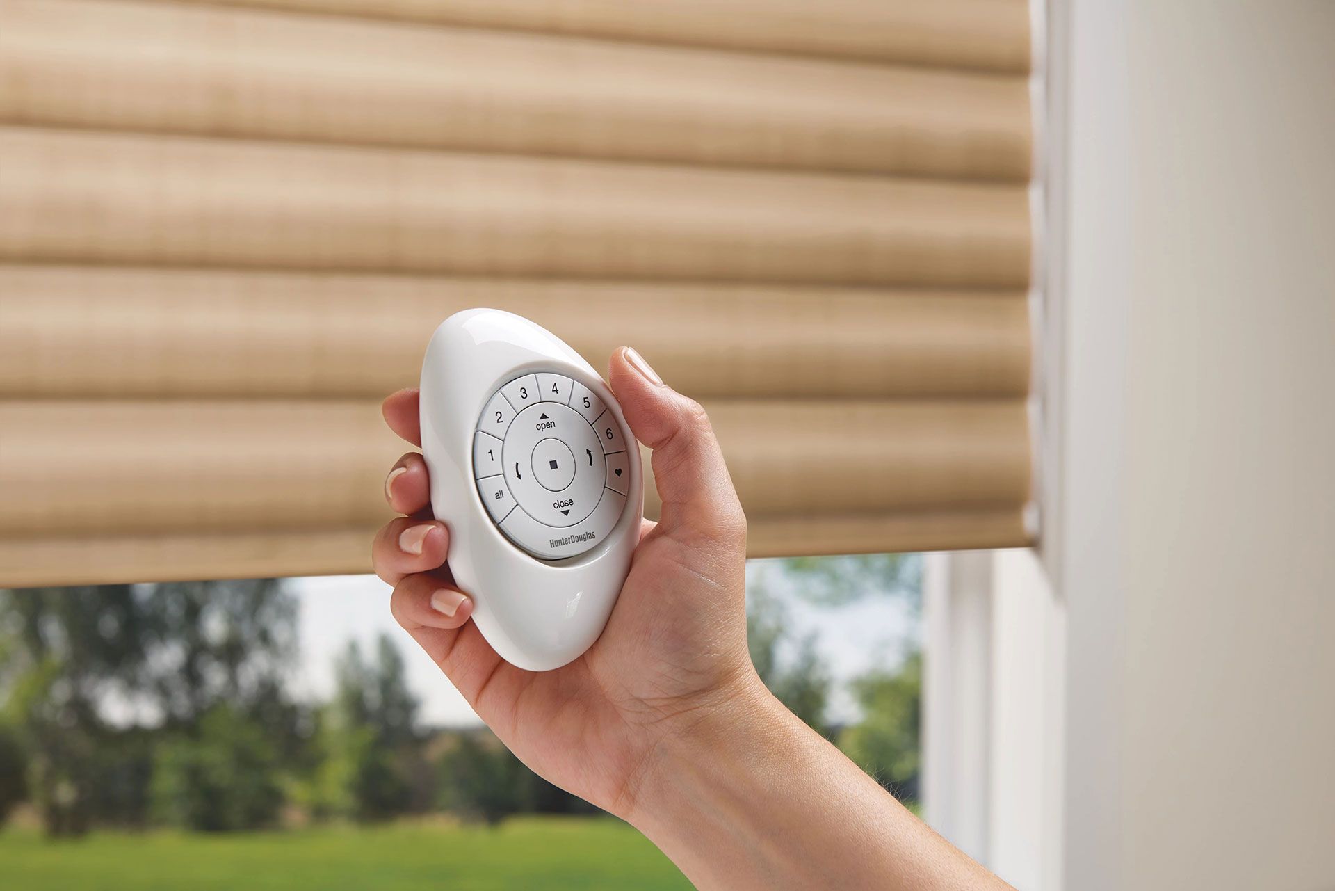 Hand holding a remote controlling a tan window blind.