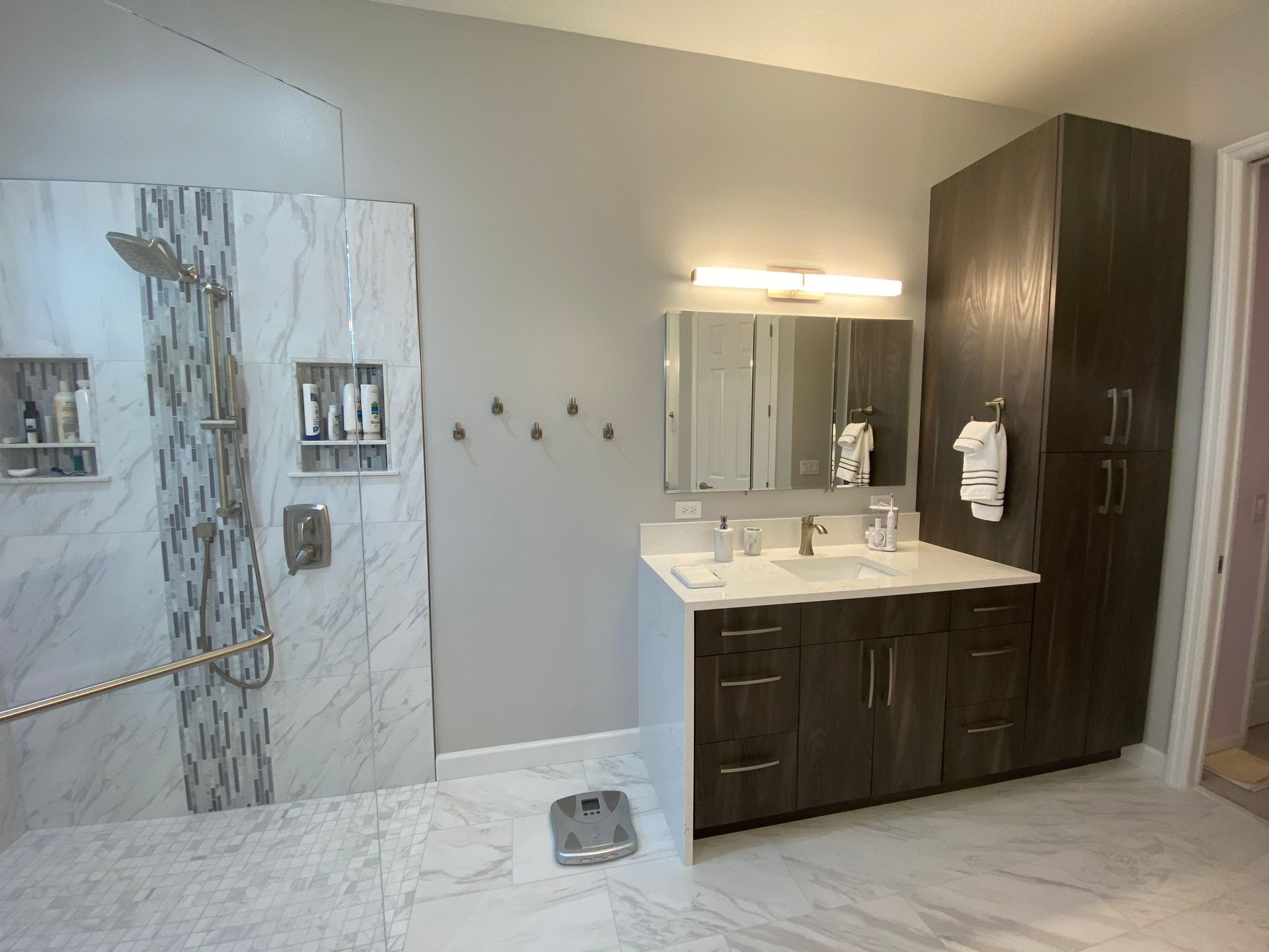 Bathroom with marble shower, gray walls, dark wood vanity, and tall cabinet.