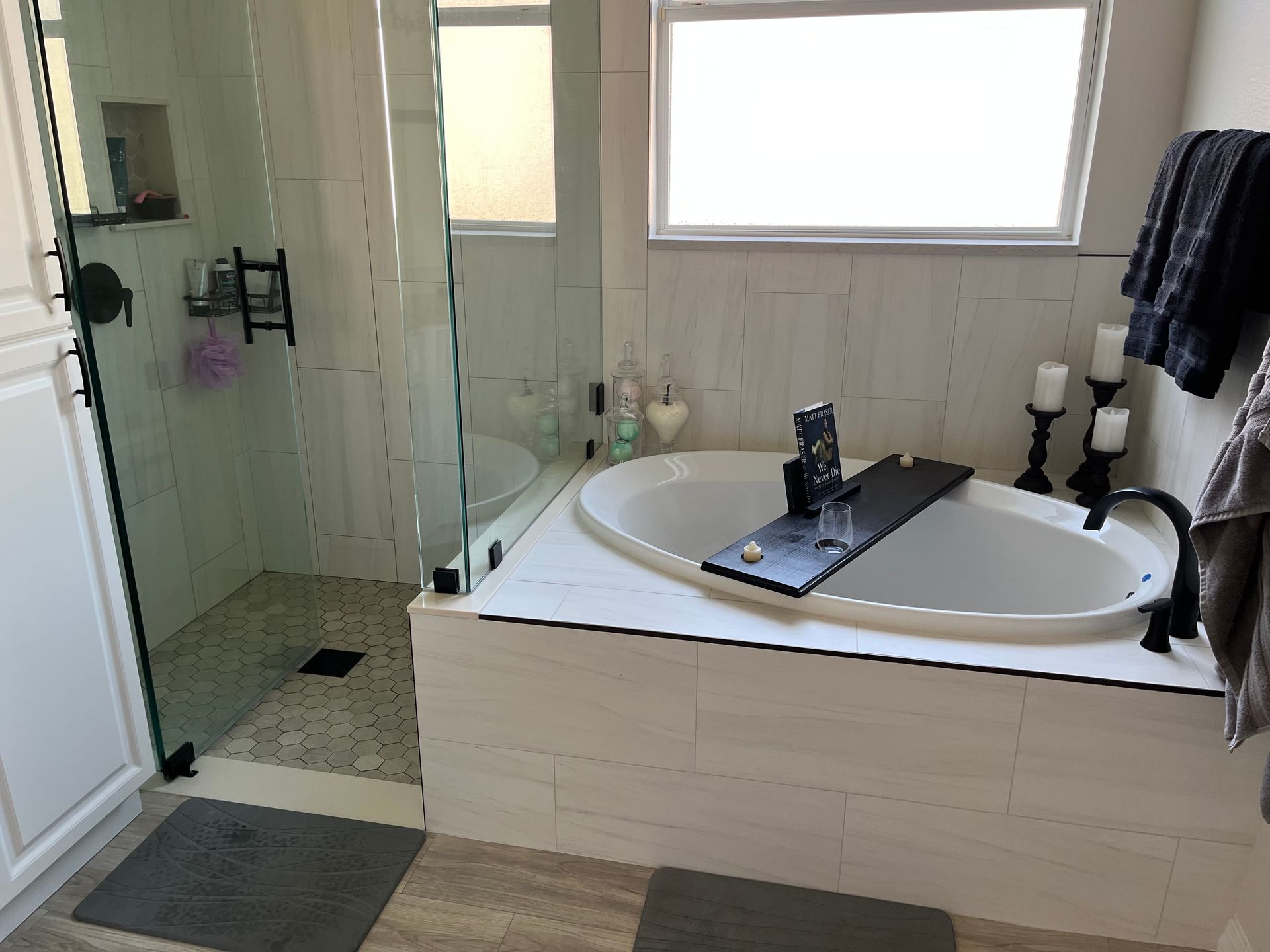 Bathroom with a white bathtub, glass shower, and white tile.